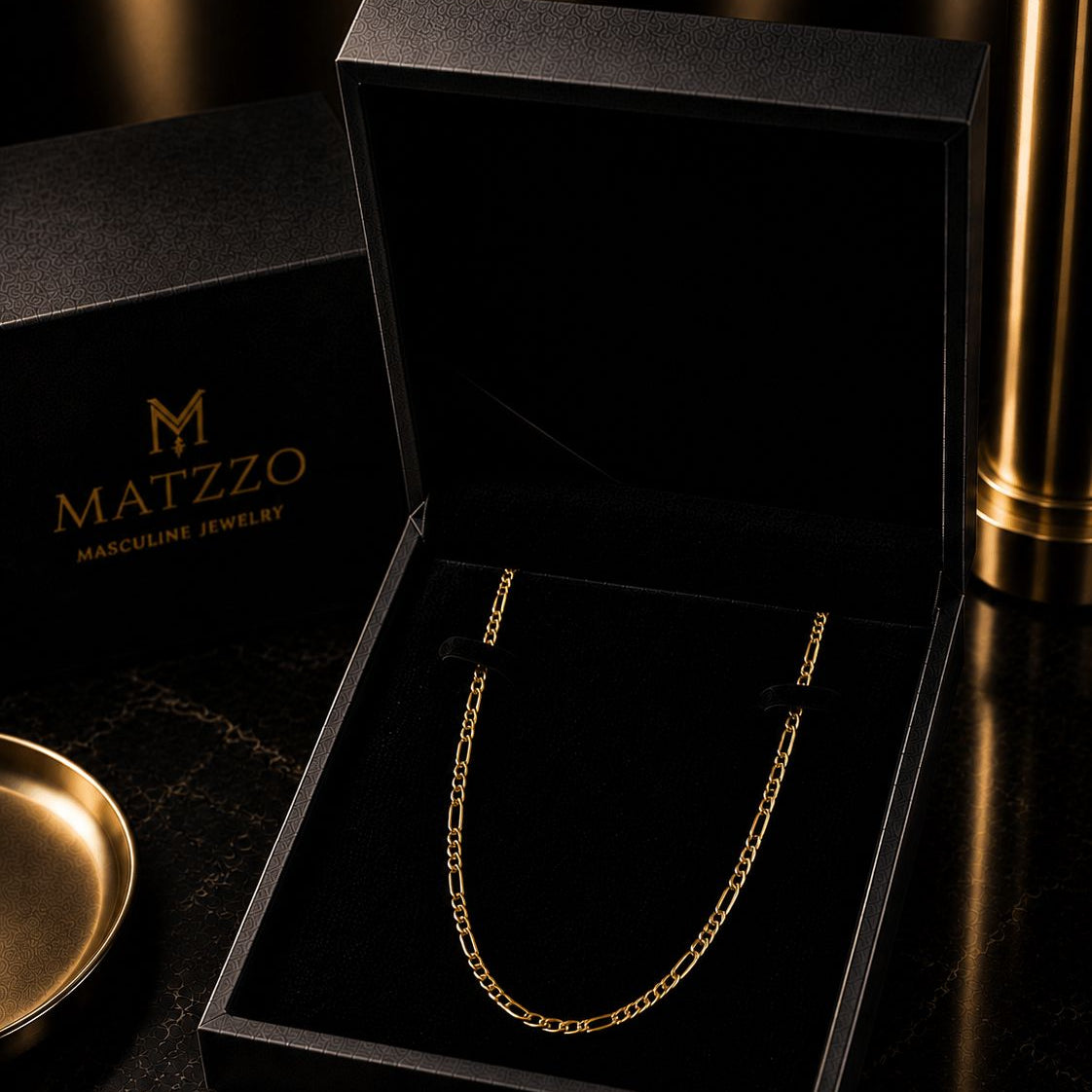 A gold chain necklace displayed inside an open black MATZZO jewelry box, with the branded black box lid and card visible around it on a dark reflective surface.